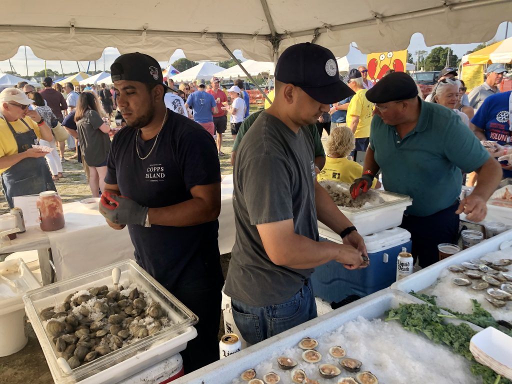 Nilson Mejia, left, and Michael Gomez, center, shuck littleneck clams and oysters at the Copps Island Oysters tent. / Photo by Thane Grauel